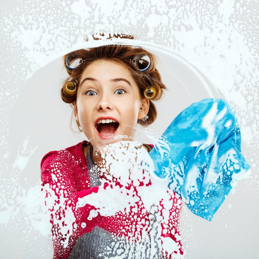 Cheerful young girl with wide smile on face washes windows in pink