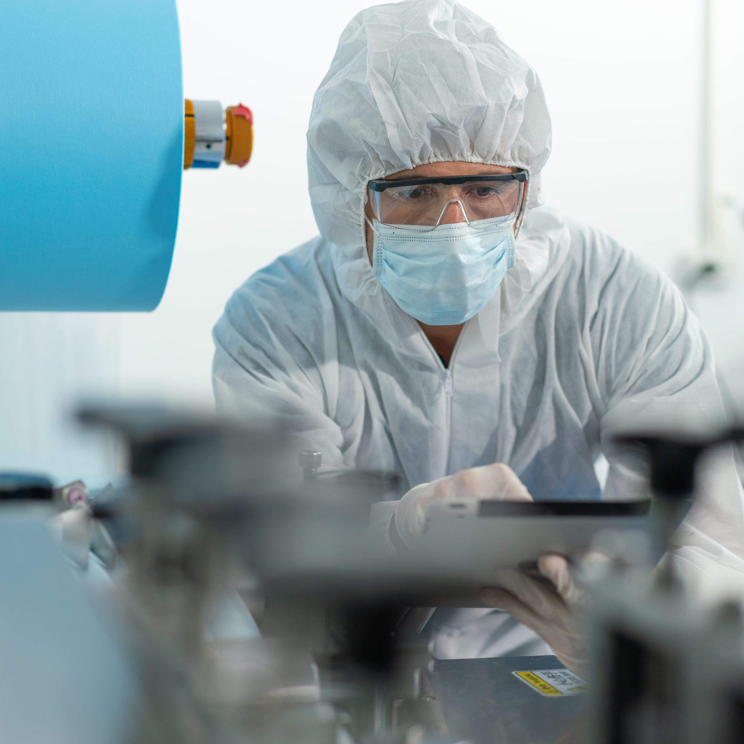 Engineer man wearing hygienic mask to protect coronavirus holding computer tablet checking and inspection machine in production line at factory industry.